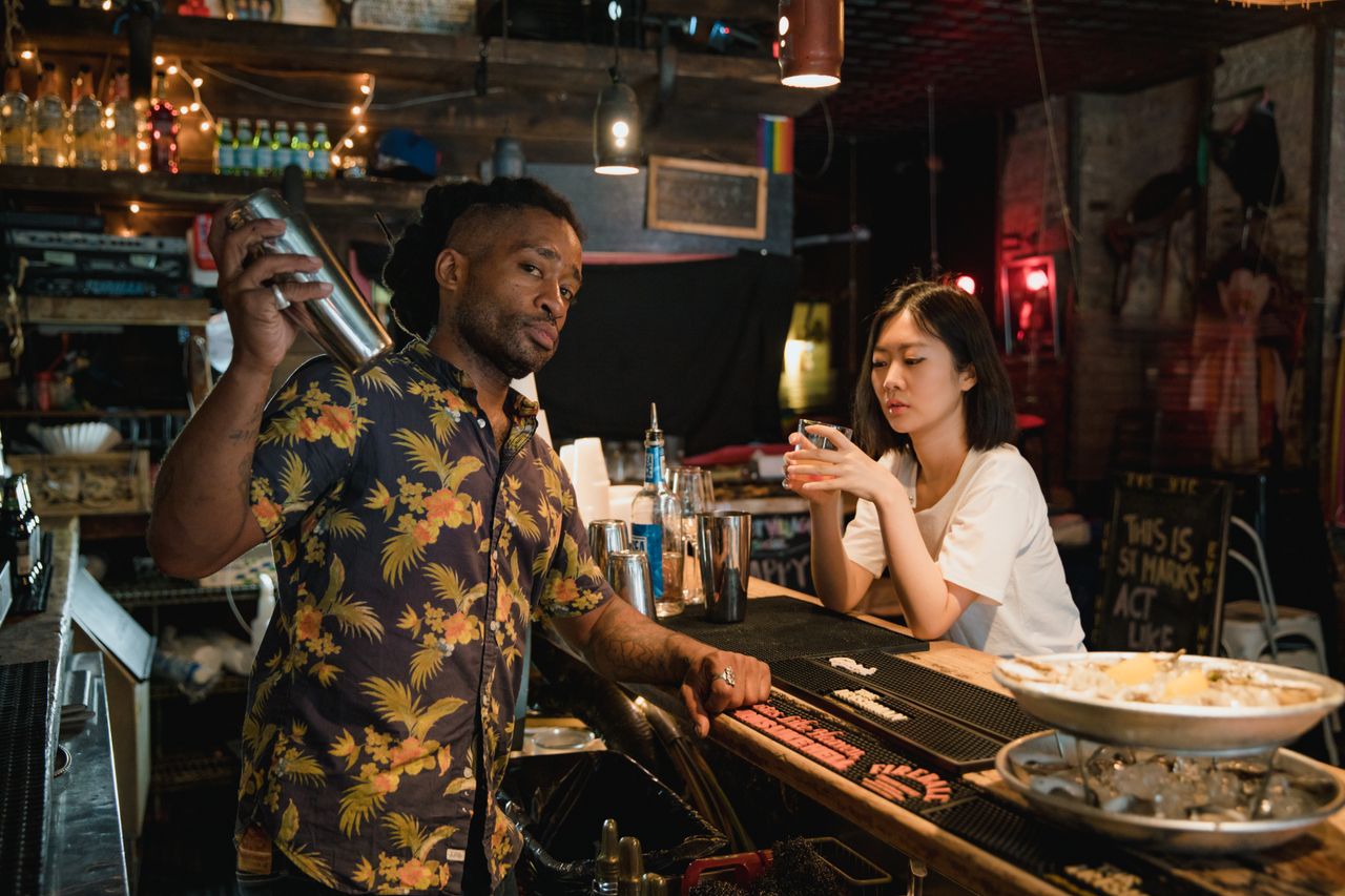services-04 A bartender in a Hawaiian shirt preparing a cocktail for a customer at a dimly lit bar.