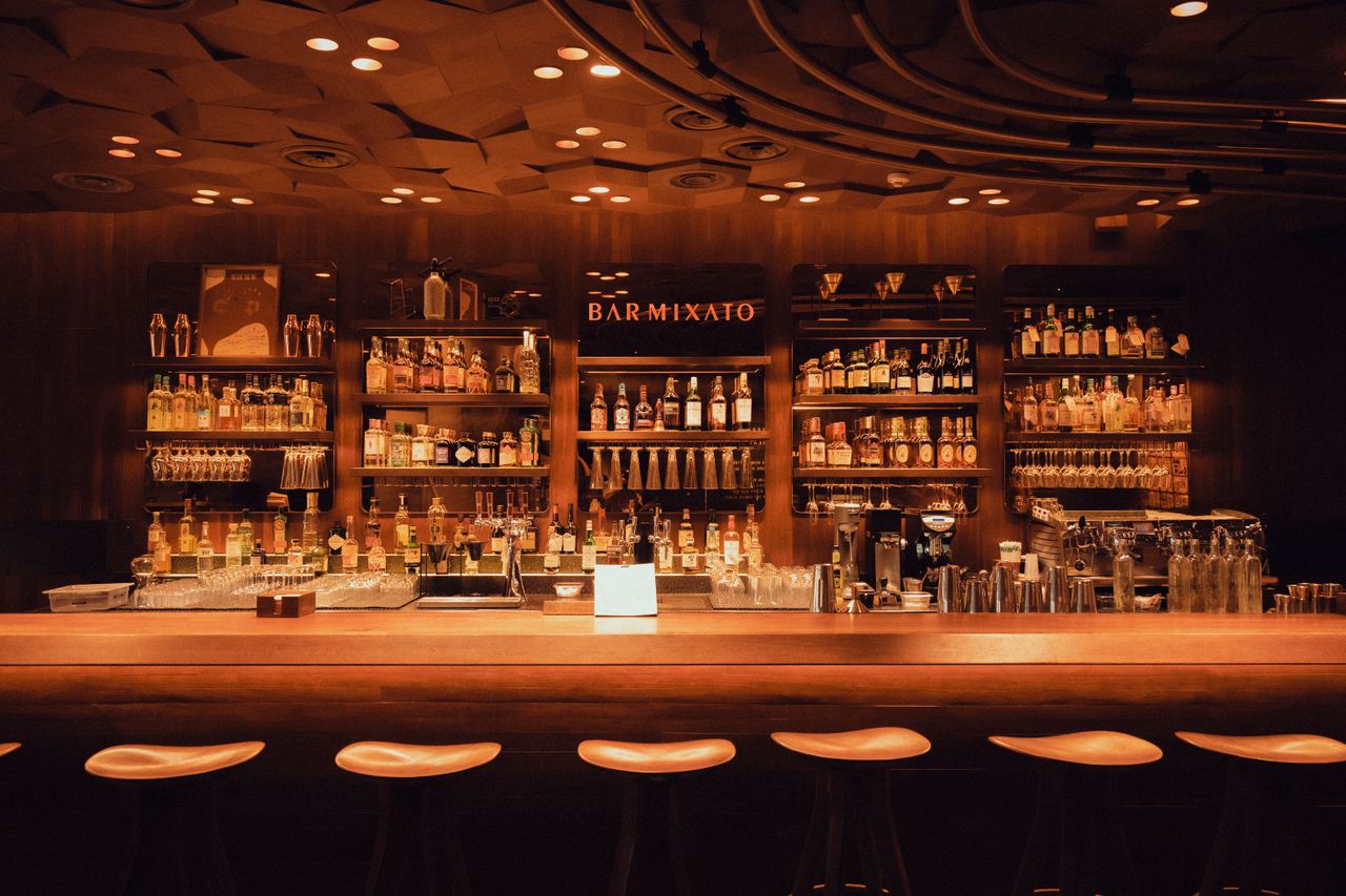 Warm, inviting bar interior with wooden decor and ambient lighting, featuring an extensive liquor collection.