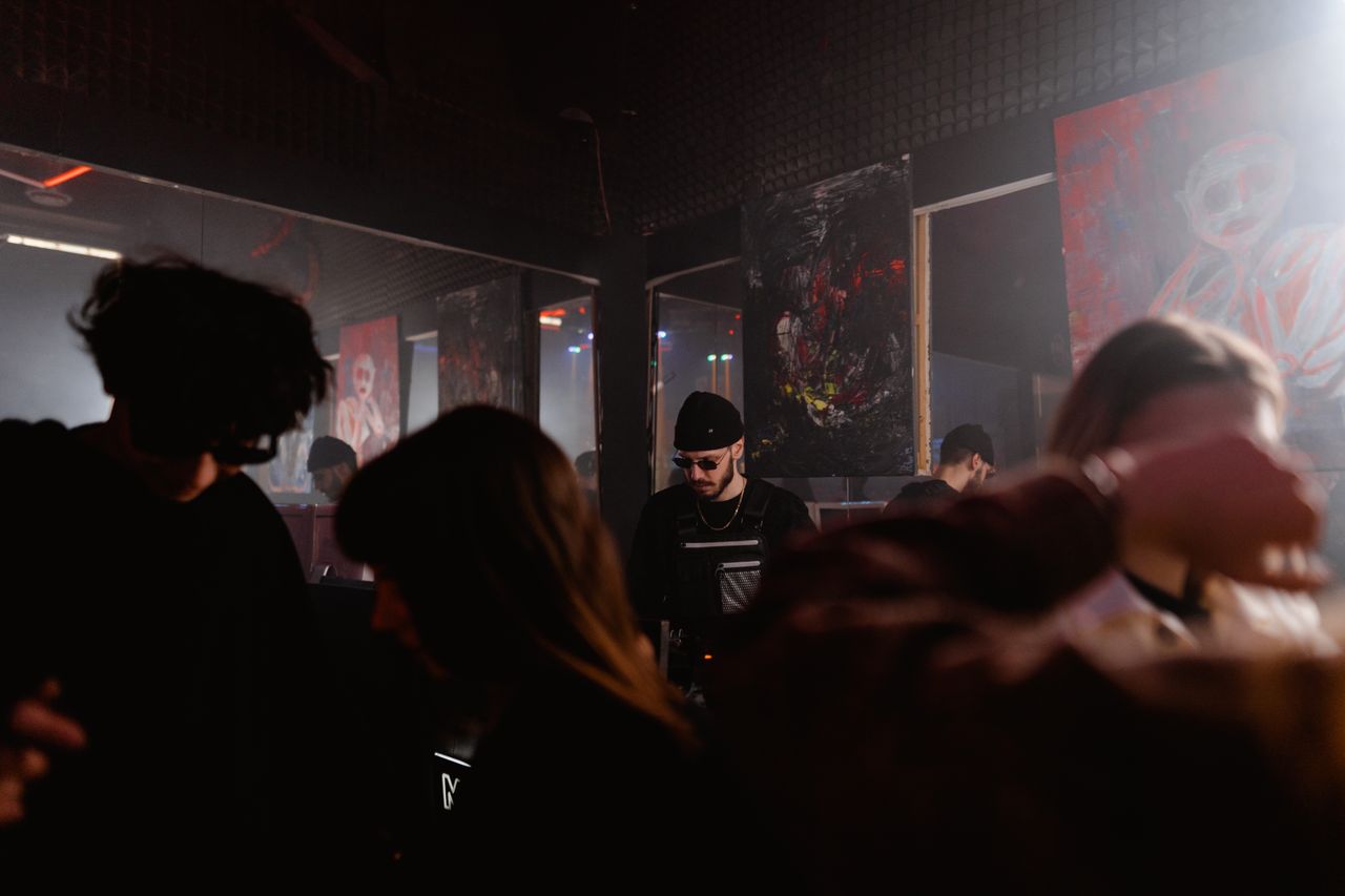 Energetic nightclub scene with a DJ and dynamic dancing crowd under moody lights.