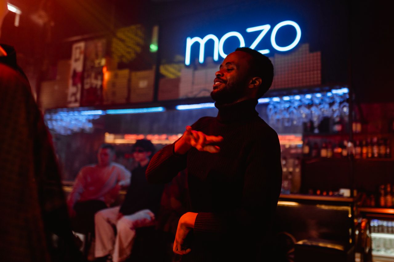 A man dances energetically under neon lights in a lively nightclub setting.