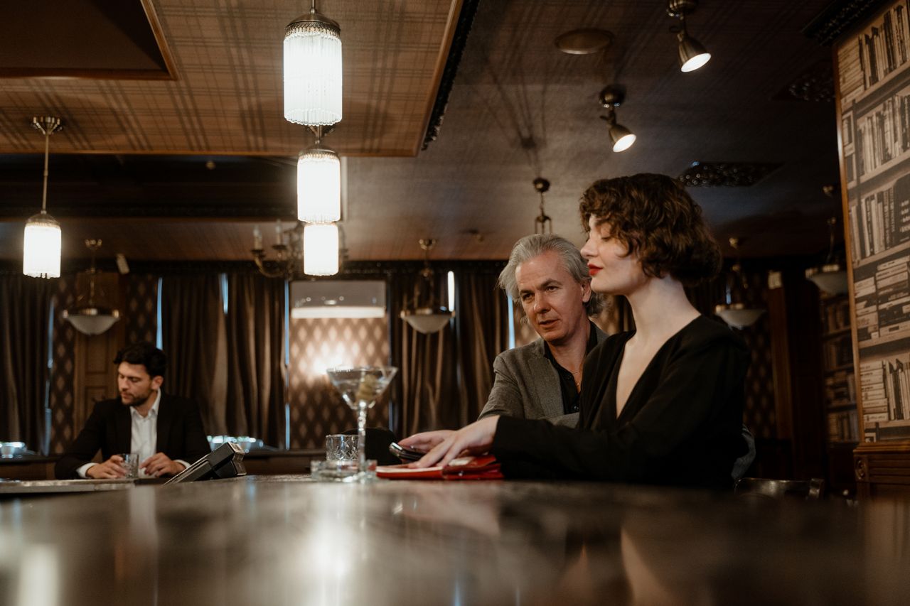 A sophisticated bar scene with two adults conversing at the counter, creating a vintage ambiance.
